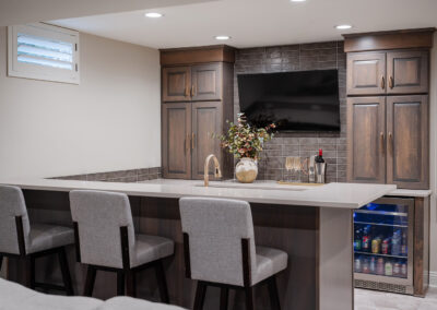 Omaha Home, Kitchen, Bathroom and Basement Remodeling - Modern home wet bar setup with dark wood cabinetry, stone backsplash, and built-in appliances, complemented by elegant bar stools. a welcoming spot for entertainment and relaxation.