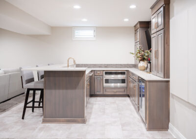 Omaha Home, Kitchen, Bathroom and Basement Remodeling - Modern kitchen interior with sleek wooden cabinetry, stainless steel appliances, an island with a sink, and tasteful lighting, in an open-concept space with a glimpse of a cozy living area.