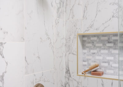Omaha Home, Kitchen, Bathroom and Basement Remodeling - Elegant bathroom corner with marble tiles featuring a brass shower head and faucet with built-in shelf for bath essentials.