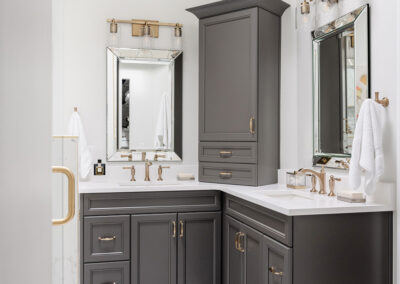Omaha Home, Kitchen, Bathroom and Basement Remodeling - A modern bathroom featuring sleek dark gray cabinetry, a white marble countertop, and dual sinks with elegant fixtures. a large mirror with sconce lighting hangs above, enhancing the bright and clean aesthetic.