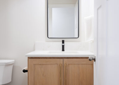 Omaha Home, Kitchen, Bathroom and Basement Remodeling - A modern bathroom vanity with wooden cabinets, a white basin, and a sleek black faucet, complemented by a rectangular mirror and an overhead pendant light.