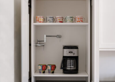 Omaha Home, Kitchen, Bathroom and Basement Remodeling - A modern kitchen cabinet with its door open, revealing an organized shelf with a coffee maker and colorful mugs. the upper shelf displays neatly arranged canned food items.