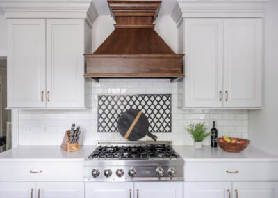 Omaha Home, Kitchen, Bathroom and Basement Remodeling - A modern kitchen featuring white cabinets, a stainless steel gas stove, and a wooden range hood above subway tile backsplash. a black circular tray and small plants decorate the countertop.